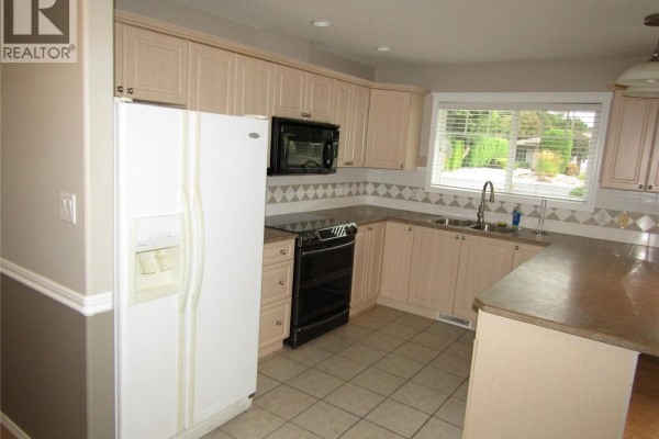 Kitchen with light wood cabinets, black appliances, and beige tiled floor. - 707 76th Avenue Unit# #5, Grand Forks