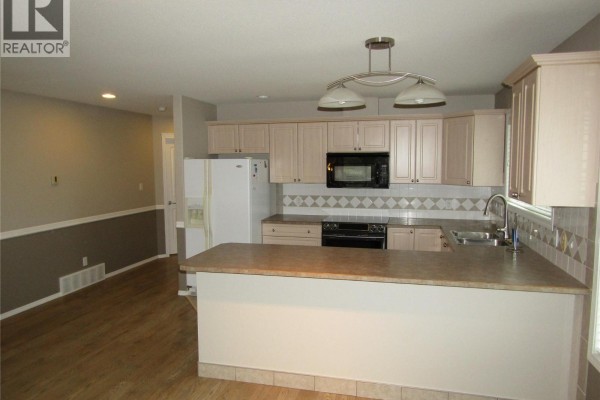 Kitchen and dining area with light wood cabinets, beige counter, and wood laminate flooring. - 707 76th Avenue Unit# #5, Grand Forks