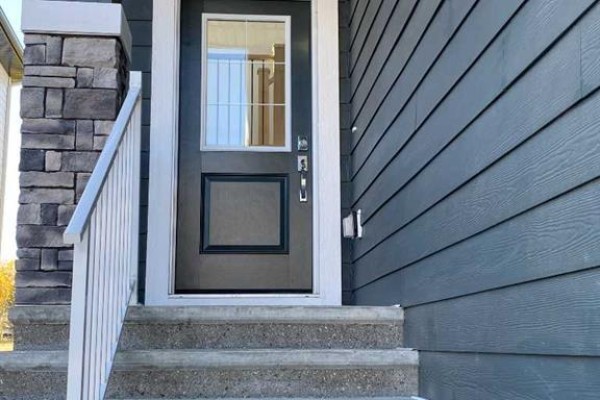 Close-up of the dark grey front door with glass and stone accents on the porch. - 707 Mandalay Avenue Nw, Carstairs