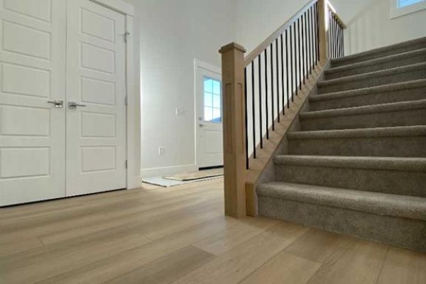 Interior entryway with light wood-look flooring, a grey carpeted staircase with black spindles, and double white doors. - 707 Mandalay Avenue Nw, Carstairs