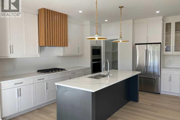Modern white kitchen with a dark grey island, stainless steel appliances, gas range, and wooden vent hood. - 707 Mandalay Avenue Nw, Carstairs