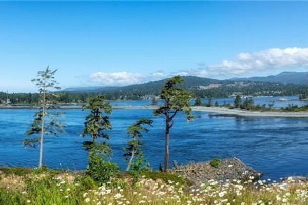Blue ocean water with forested shoreline and hills in the distance. - 7078 East Sooke Rd, Sooke