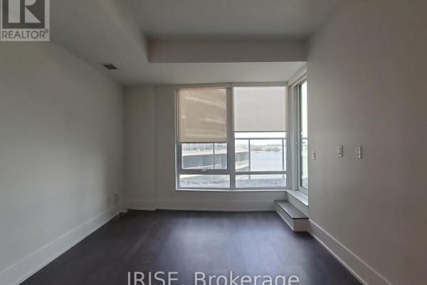 Empty room with dark wood floors and a large window with a view of the lake. - 708 - 1 Edgewater Drive, Toronto