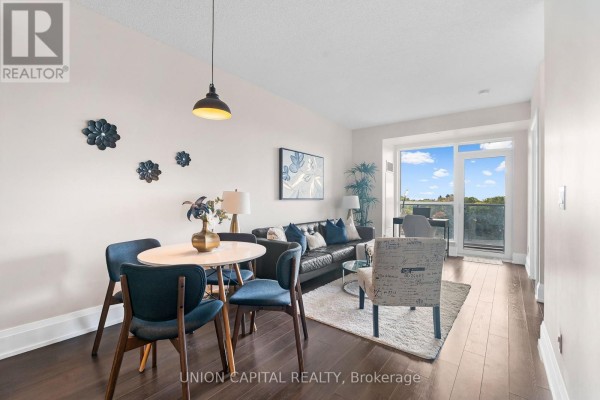 Living area with a black leather sofa, armchair, coffee table, and a small dining table, with a balcony door and window overlooking the city. - 708 - 120 Harrison Garden Boulevard, Toronto