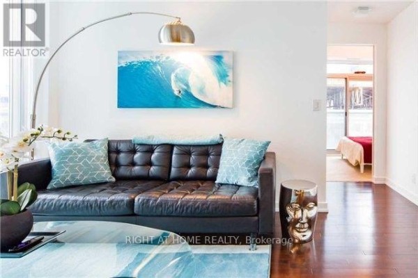 Living room area with a black leather sofa, patterned pillows, and view into a bedroom. - 708 - 14 York Street, Toronto