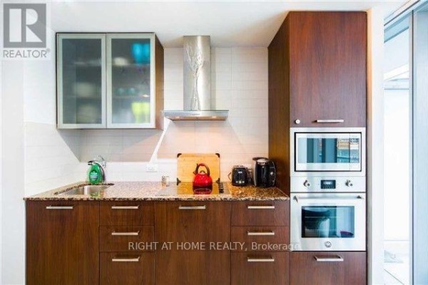 Modern kitchen with dark wood cabinets, granite countertops, and stainless steel appliances. - 708 - 14 York Street, Toronto