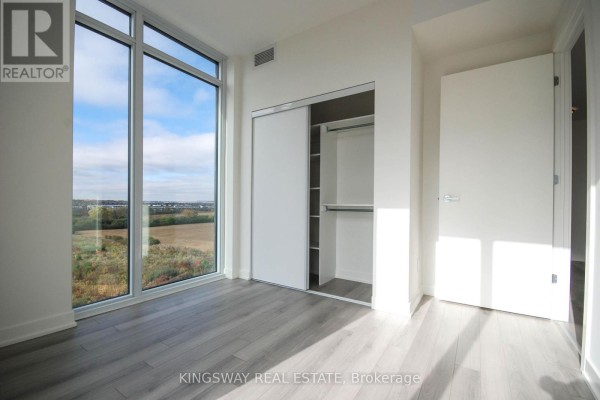 Bedroom with a large window, grey laminate floor, and a white sliding door closet. - 708 - 3071 Trafalgar Road, Oakville