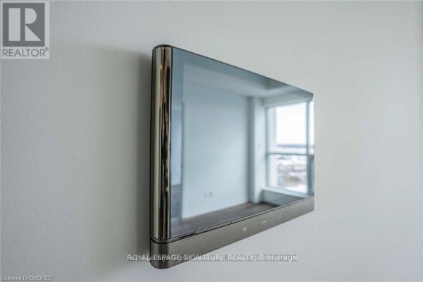 Modern smart home control panel mounted on a white wall reflecting a bright room with a window. - 708 - 405 Dundas Street W, Oakville