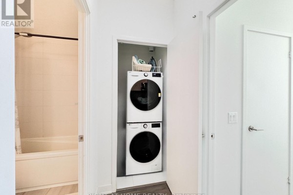 Hallway closet with stacked white washer and dryer, adjacent to a bathtub. - 708 - 681 Yonge Street, Barrie