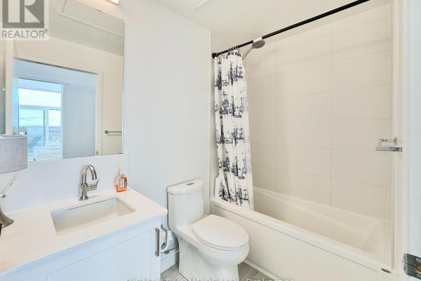 Bathroom with a white vanity, toilet, and bathtub with a patterned shower curtain. - 708 - 681 Yonge Street, Barrie