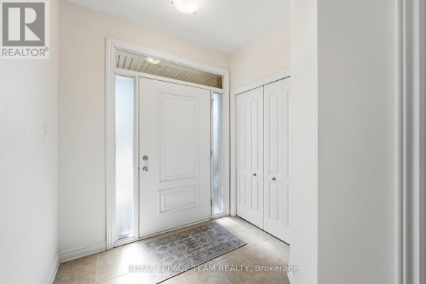 Bright entryway with a white front door, tiled floor, and double bi-fold closet doors. - 708 Eagle Crest Heights, Ottawa