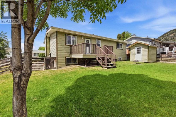 Rear exterior view of a light green house with a wooden deck and a small shed in the backyard. - 708 Smith Street, Williams Lake