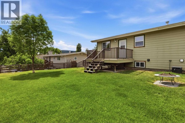 Backyard view of a light green house with a wooden deck, a shed, and a wooden fence. - 708 Smith Street, Williams Lake