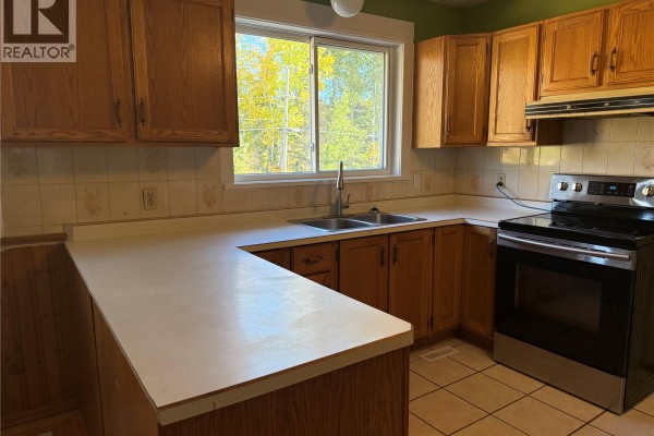 Kitchen features light wood cabinets, white countertops, and a stainless steel stove. - 708 Studer Street, La Ronge