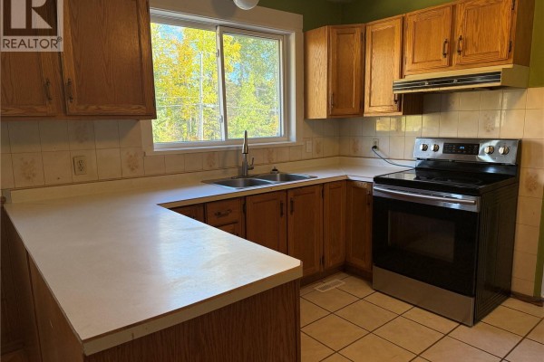 Corner view of a kitchen with wood cabinets, white counters, and stainless steel appliances. - 708 Studer Street, La Ronge
