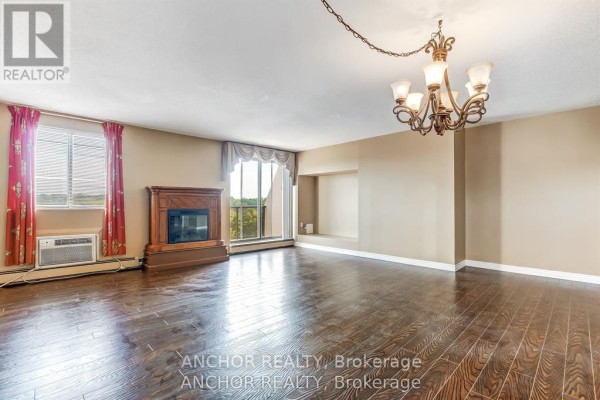 Living room with hardwood floors, fireplace, large windows, and chandelier. - 709 - 1255 Commissioners Road W, London South