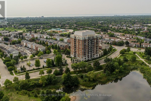 Aerial view of an apartment building with a pond in the foreground and surrounding neighbourhood. - 709 - 2325 Central Park Drive, Oakville