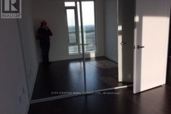 A person taking a photo in a bedroom with dark hardwood floors and a large window. - 709 - 2560 Eglinton Avenue W, Mississauga