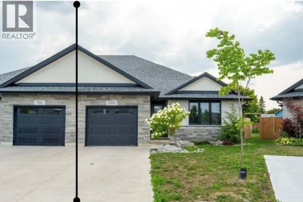Open concept living space with vaulted ceiling, kitchen island, fireplace, and patio doors. - 709 Ferdinands Crescent, Sarnia