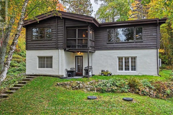 Front view of a house with a red front door, white stucco lower level, and stone landscaping. - 709 Macpherson Drive, East Ferris