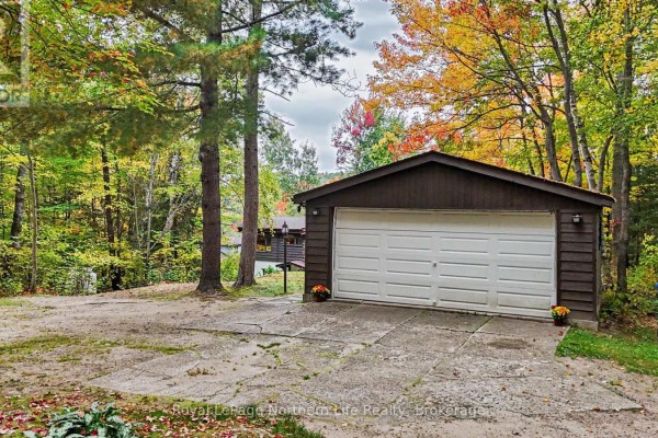 A detached brown garage with a white door sits on a concrete driveway. - 709 Macpherson Drive, East Ferris