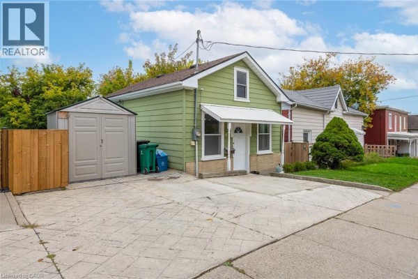 Front of the green house exterior with driveway, shed, and nearby homes. - 71 Beverly Street, Cambridge