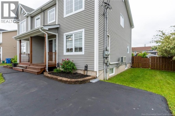 Side view of a grey townhouse showing the driveway, grass, wooden fence, and exterior utilities. - 71 Houlahan Street, Dieppe