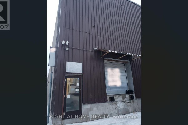 Dark metal commercial building exterior with a glass door, metal roll-up door, and utility boxes. - 71 Howden Road, Toronto