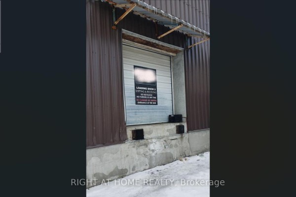 Close-up of a loading dock with a raised metal roll-up door and concrete bumpers on the ground. - 71 Howden Road, Toronto