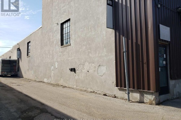 Side view of a commercial building with stucco and corrugated metal siding, a loading dock, and a truck. - 71 Howden Road, Toronto