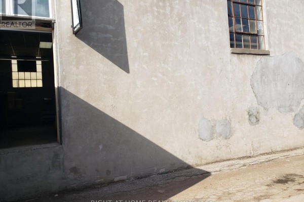 Exterior wall of a building with stucco finish, a doorway, windows, and shadows cast by the sun. - 71 Howden Road, Toronto