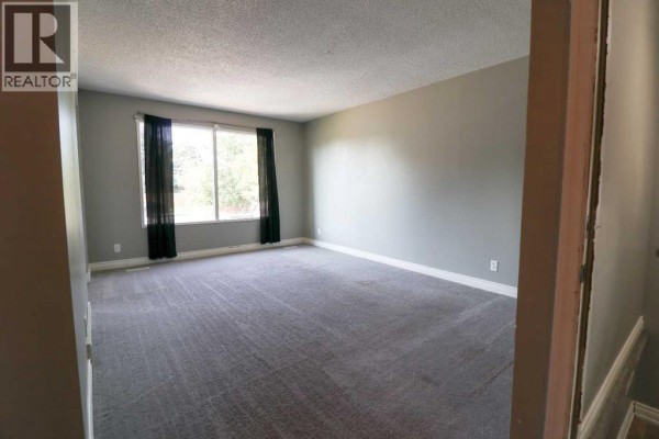 Living room with grey walls, grey carpet, and a large window with black curtains. - 71 Laval Boulevard W, Lethbridge