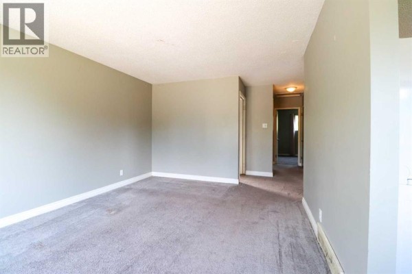 Living room with grey walls and grey carpet, looking down a hallway with carpeted floors. - 71 Laval Boulevard W, Lethbridge