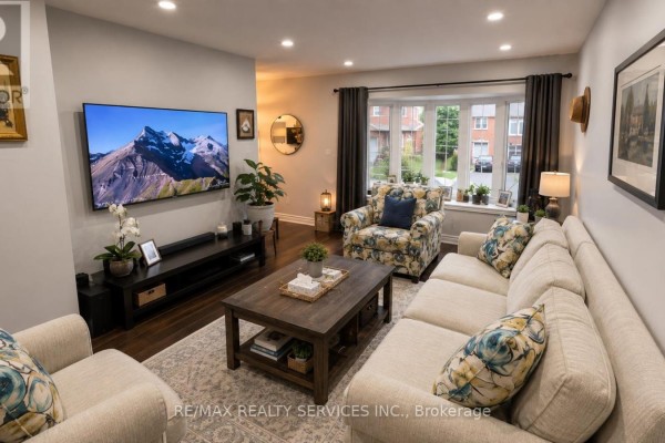 Living room with sectional, armchair, bay window view of street, and mounted television. - 71 Newlyn Crescent, Brampton