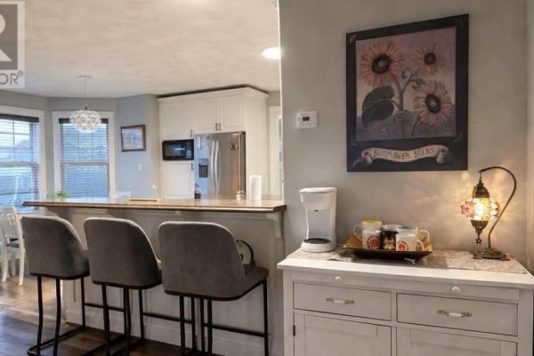 Kitchen island with grey bar stools and a view of stainless steel appliances and white cabinetry. - 71 Rebecca Drive, Summerside