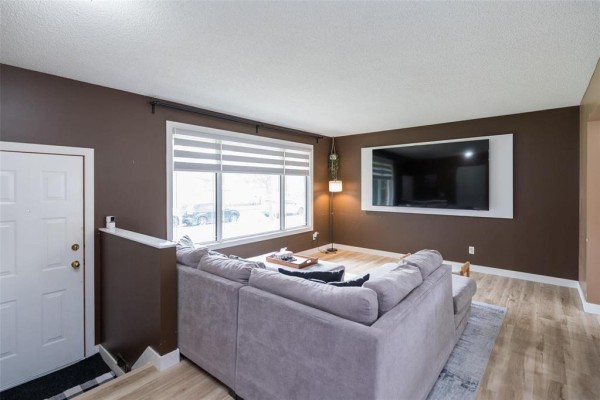 Living room with a large sectional sofa, ottoman, coffee table, and mounted television against brown walls. - 71 Rougeau Avenue, Winnipeg