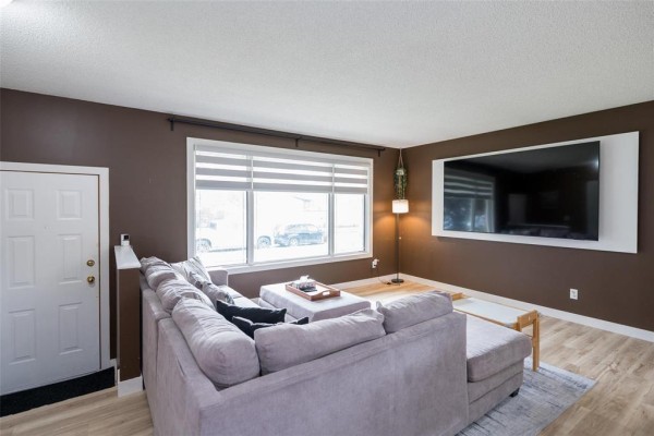 Living room featuring a grey sectional sofa, ottoman, and a large window with striped blinds. - 71 Rougeau Avenue, Winnipeg