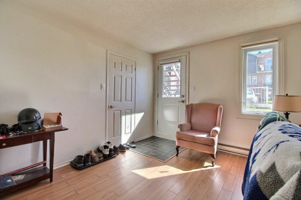 Apartment entryway with a pink armchair, shoe rack, and a window looking outside. - 71 Rue De Sauternes, #1, Gatineau