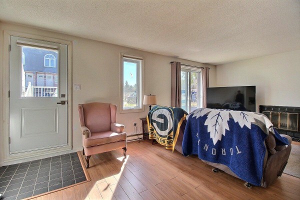 Living room with a pink armchair, fireplace, large TV, and sliding doors. - 71 Rue De Sauternes, #1, Gatineau