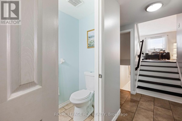 Powder room with a white toilet, light blue walls, and a tiled floor. - 71 Shirley Street, Orangeville