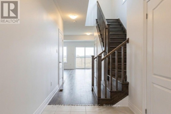 Interior hallway with a dark wood staircase leading upstairs and tiled flooring. - 71 Sunset Way, Thorold