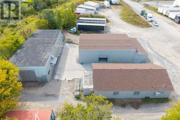 Aerial view of commercial buildings on a lot with surrounding vegetation and a river in the distance. - 71 Wolfe Street, Quinte West