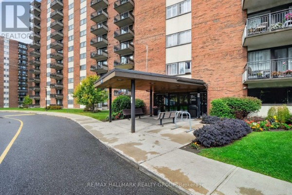 Covered building entrance with benches and planters leading to glass doors with the address 1485. - 710 - 1485 Baseline Road, Ottawa