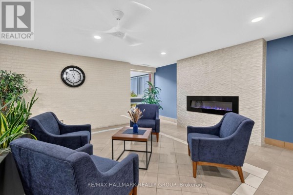 Lobby seating area with dark blue armchairs, a coffee table, and a decorative modern fireplace. - 710 - 1485 Baseline Road, Ottawa
