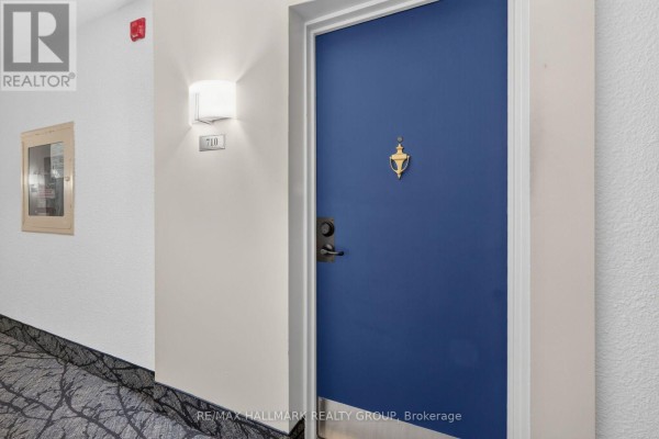 Apartment door number 710 on a bright blue door with a brass knocker and a light fixture. - 710 - 1485 Baseline Road, Ottawa
