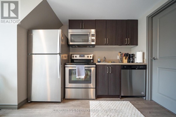 Compact kitchen with dark wood cabinets, stainless steel appliances, and light wood floor. - 710 - 321 Spruce Street, Waterloo