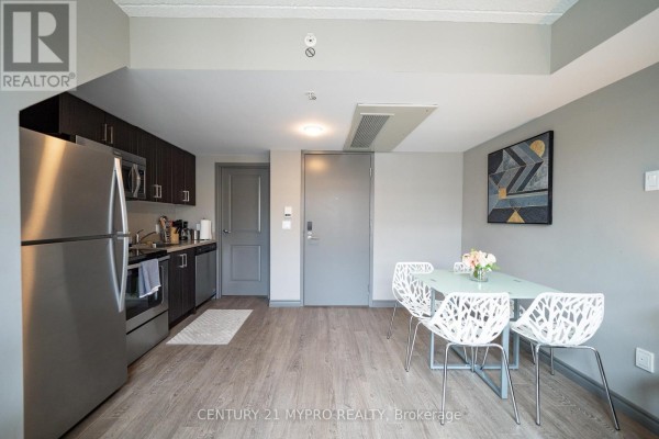 Open-concept kitchen and dining area with white chairs and grey walls. - 710 - 321 Spruce Street, Waterloo