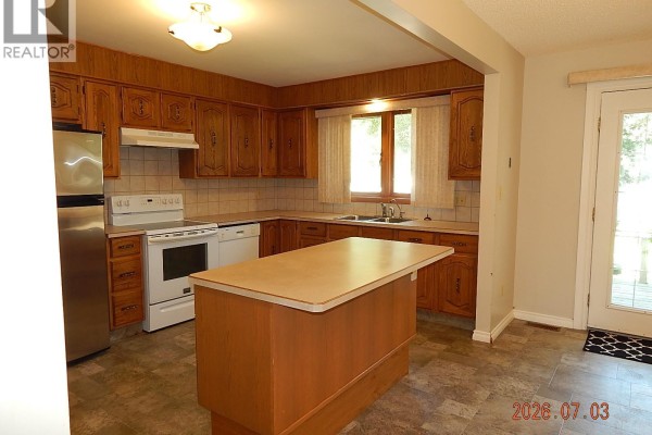 Living room with light beige walls, hardwood floors, and an opening to another room. - 710 3rd Street E, Assiniboia