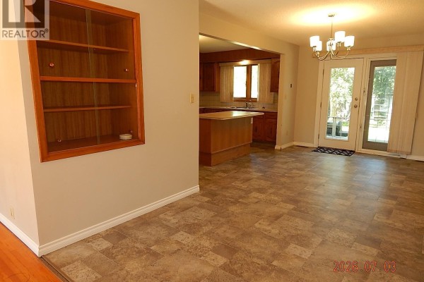 Kitchen with wood cabinets, white appliances, an island, and a window with curtains. - 710 3rd Street E, Assiniboia
