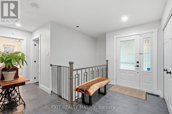 Interior foyer with gray tile floor, white walls, a metal railing, and a wooden bench. - 710 Du Parc Road, Champlain